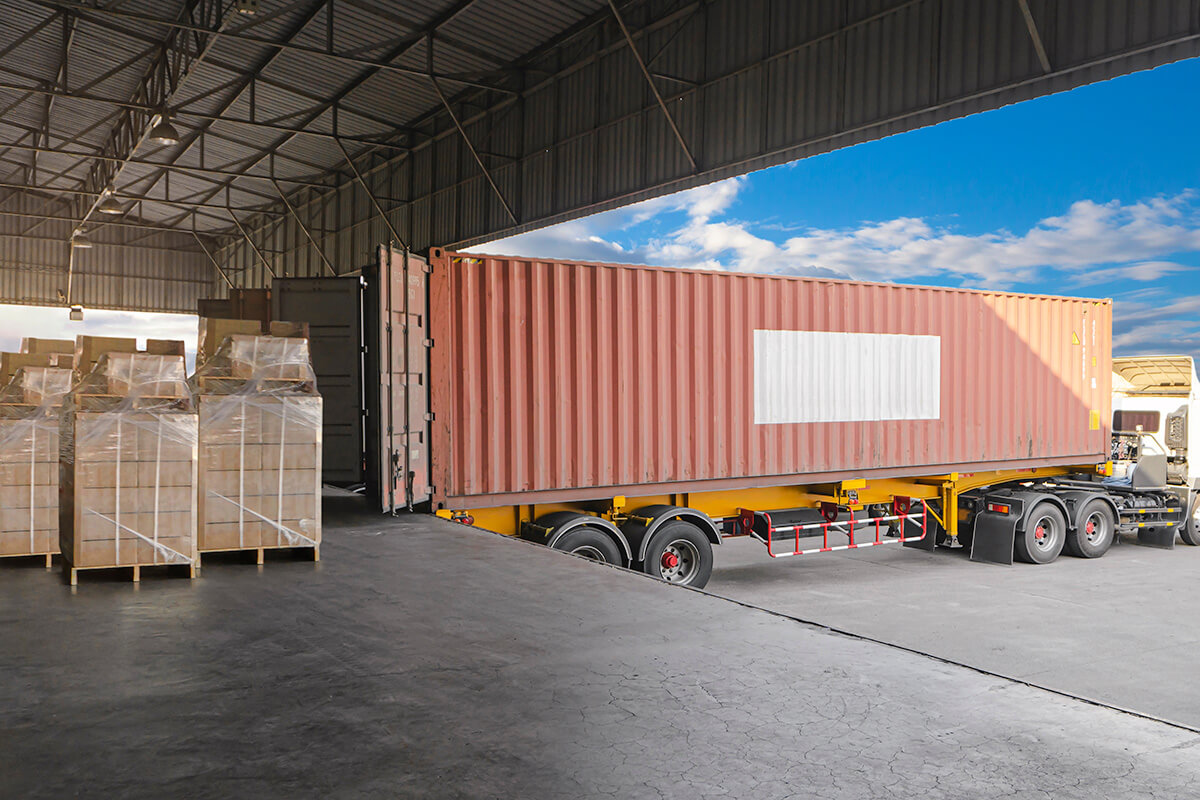 Shipping truck parked near warehouse facility with shipping container door opened.